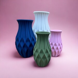 May include: Four ceramic vases in different colors and sizes. The vases have a geometric pattern and are arranged on a pink background.