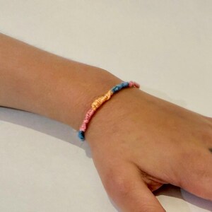 May include: A colorful friendship bracelet with blue, pink, and orange threads woven together.