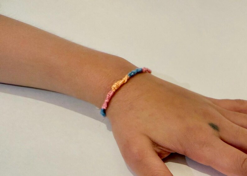 May include: A colorful friendship bracelet with blue, pink, and orange threads woven together.