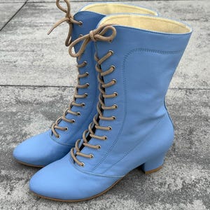 Könnte beinhalten: Ein Paar hellblaue Lederstiefel mit Schnürung und niedrigem Blockabsatz. Die Stiefel haben eine spitze Zehenpartie und sind mit braunen Schnürsenkeln gebunden.