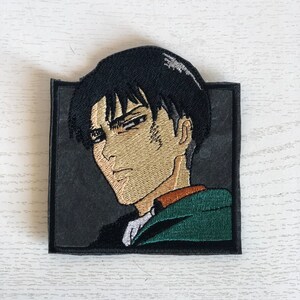 May include: Embroidered patch featuring a black-haired anime character with a serious expression. The character is wearing a green and brown jacket. The patch is surrounded by a black border.