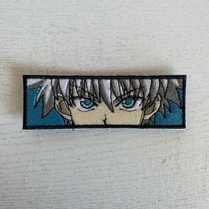 May include: A white-haired anime character with blue eyes is featured on a blue and white embroidered patch. The character's eyes are wide open and staring directly at the viewer.