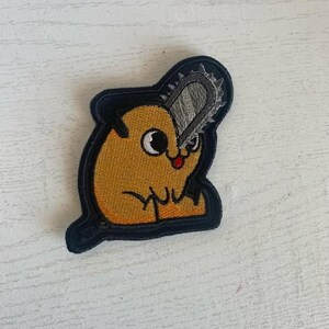 May include: A yellow cartoon hamster with a chainsaw for a head. The hamster is wearing a black outline and has a red mouth and black eyes. The chainsaw is silver and has a black handle.
