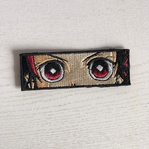 May include: Embroidered patch featuring a close-up of a pair of anime eyes with red irises and white pupils. The eyes are surrounded by a black border.