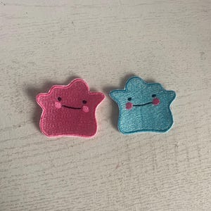 May include: Two embroidered patches, one pink and one blue, shaped like a star with a smiling face.
