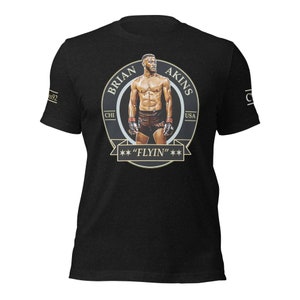 May include: Black t-shirt featuring a circular graphic of a muscular man with the text "BRIAN AKINS" and "FLYIN". The graphic includes the text "CHI USA". The shirt has short sleeves.