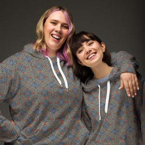 May include: Two people wearing blue and yellow patterned hoodies with white drawstrings. The hoodies have a geometric pattern of circles and squares.