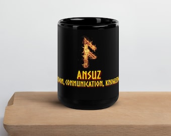 Puede incluir: Taza de cerámica negra con un símbolo de runa naranja ardiente y el texto "Ansuz, Sabiduría, Comunicación, Conocimiento".