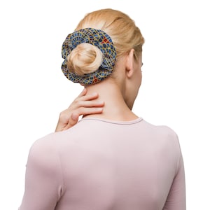 May include: A blue and gold patterned hair scrunchie with red accents. The scrunchie is worn in a woman's hair.