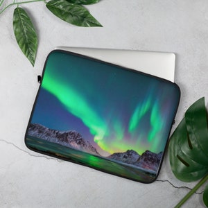 May include: A laptop sleeve featuring a vibrant green and purple aurora borealis over a snow-capped mountain range. The aurora is reflected in the water below.