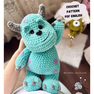 Könnte beinhalten: Eine türkisfarbene gehäkelte Monsterpuppe mit grauen Hörnern, Füßen und Händen sowie lila Flecken. Die Puppe hat schwarze Augen und einen lächelnden Mund. Der Text auf dem Bild lautet "CROCHET PATTERN PDF ENGLISH".