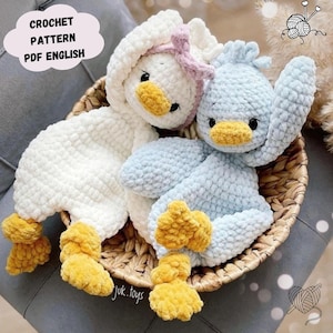 Può includere: Due giocattoli di peluche a forma di anatra all'uncinetto, uno bianco e uno azzurro chiaro, con becchi e piedi gialli. I giocattoli sono in un cesto di vimini.