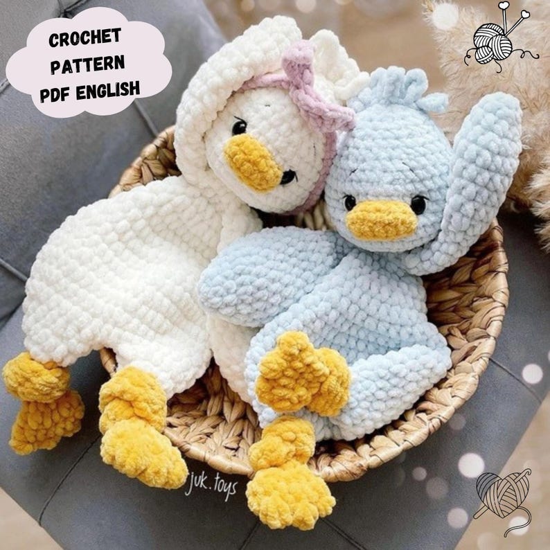 Op de afbeelding: Twee gehaakte pluche eendenspeelgoedjes, een wit en een lichtblauw, met gele snavels en pootjes. De speelgoedjes liggen in een rieten mand.