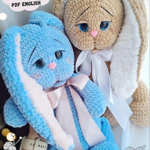 May include: Two crocheted bunny plushies, one blue and one beige, with white fur accents on the ears. Both bunnies have pink noses and blue eyes. The blue bunny has a pink ribbon around its neck. The text "CROCHET PATTERN PDF ENGLISH" is visible in the top left corner of the image.