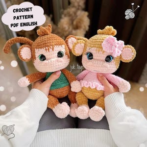 May include: Two crocheted monkey toys, one brown with a green shirt and one tan with a pink shirt and a pink bow. The toys are sitting on a person's lap.
