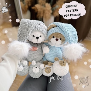Pode incluir: Dois ursos de peluche de crochê usando gorros de dormir de crochê. O urso à esquerda é cinza e o urso à direita é azul. Os ursos estão segurando animais de pelúcia de crochê.