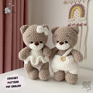 May include: Two crocheted teddy bears, one wearing a white dress with a bow and the other wearing a white overall with a button. Both bears have brown fur and black eyes.