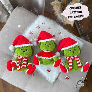 Könnte beinhalten: Drei gehäkelte grüne Figuren mit roten Weihnachtsmützen und passenden rot-weiß gestreiften Schals. Jede Figur hat ein rotes Hemd und rote Füße. Der Text "CROCHET PATTERN PDF ENGLISH" befindet sich in einer weißen Sprechblase.