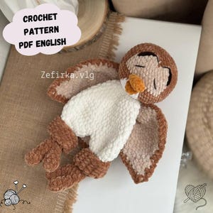 Op de afbeelding: Een gehaakte uil in bruin, crème en oranje tinten. De uil heeft gesloten ogen, een pluizige witte borst en uitgestrekte vleugels. De afbeelding bevat de tekst "CROCHET PATTERN PDF ENGLISH" en "Zefirka.vlg".