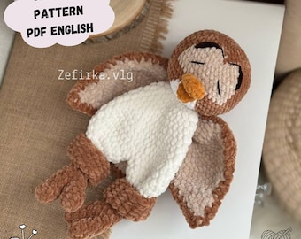 May include: A handmade crochet owl in shades of brown, cream, and orange. The owl has closed eyes, a fluffy white chest, and outstretched wings. Text on the image reads "CROCHET PATTERN PDF ENGLISH" and "Zefirka.vlg".