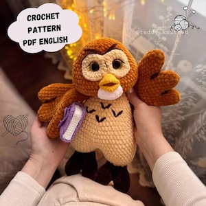 Puede incluir: Un peluche de búho tejido a ganchillo en tonos marrón, beige y blanco, sosteniendo un pequeño libro morado. El búho tiene ojos grandes y un pico amarillo. El texto en la imagen dice "CROCHET PATTERN PDF ENGLISH".