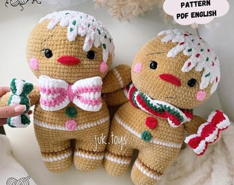May include: Two crocheted gingerbread man dolls. The dolls are tan with white icing, red lips, and pink cheeks. One doll has a pink and white bow tie, and the other has a red, green, and white scarf. The text "CROCHET PATTERN PDF ENGLISH" is in the image.