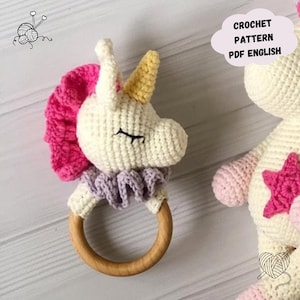 May include: Crochet pattern for a unicorn rattle toy with a wooden ring. The unicorn is white with pink and purple accents. The pattern is in PDF format and is in English.