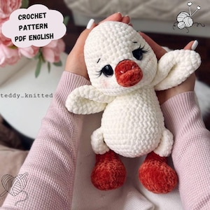 May include: A handmade white crochet duck with red feet and beak is held in the hands. The duck has black eyes with long eyelashes. Text on the image reads "CROCHET PATTERN PDF ENGLISH".