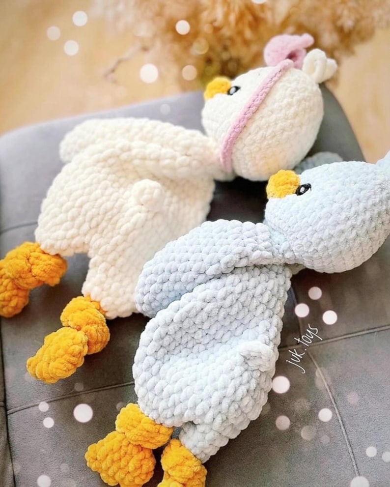 Op de afbeelding: Twee gehaakte knuffels in de vorm van vogels. E&eacute;n is wit met een roze strik en de andere is lichtblauw. Beide hebben gele voeten.
