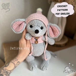 Könnte beinhalten: Häkelanleitung PDF in Englisch für eine graue und rosa Amigurumi-Maus mit einem rosa Hut und einer Weste. Die Maus hat einen kleinen, braunen Knopf auf ihrer Weste.