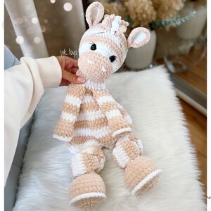 May include: A handmade, plush zebra toy in cream and tan stripes. The stuffed animal has a soft, textured appearance with a white mane and small, rounded ears. The toy is designed with black eyes and is suitable for children.