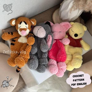 May include: A collection of four crocheted plush toys: Tigger, Eeyore, Piglet, and Winnie the Pooh. Tigger is orange with black stripes, Eeyore is gray, Piglet is pink, and Winnie the Pooh is yellow. The toys are handmade and soft, with the text "Crochet Pattern PDF English".