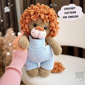May include: Crocheted lion amigurumi toy wearing blue overalls. The lion has a fluffy orange mane and tail. The image includes the text "CROCHET PATTERN PDF ENGLISH".