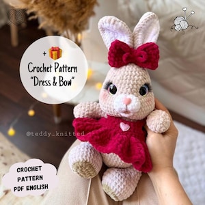 May include: Crochet pattern for a pink bunny wearing a red dress and a red bow. The pattern is called "Dress & Bow" and is available in English. The pattern is available for purchase on Etsy.