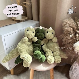 May include: Three crocheted dinosaur plushies in green and light green colors sitting on a chair. The plushies are made with a soft, fuzzy yarn. The image includes the text "CROCHET PATTERN PDF ENGLISH".