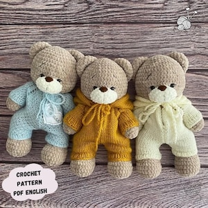 May include: Three crocheted teddy bears wearing different coloured outfits. The bear on the left is wearing a light blue outfit, the middle bear is wearing a yellow outfit, and the bear on the right is wearing a cream coloured outfit. The bears are sitting on a wooden surface. Crochet pattern PDF English.