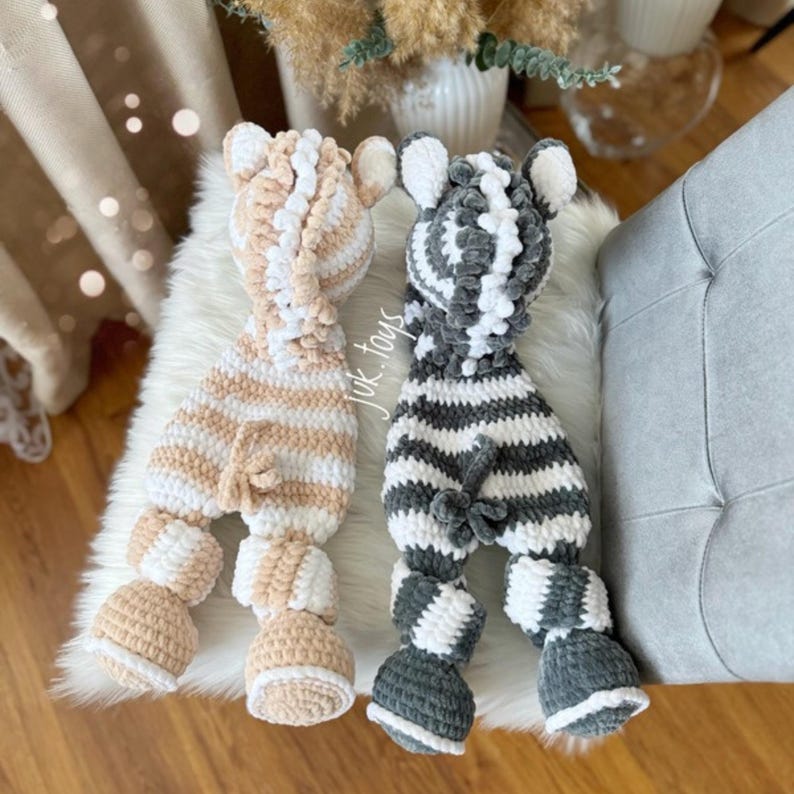 May include: Two handmade crochet animal toys, one beige and white striped, the other gray and white striped. The toys have floppy ears, rounded heads, and four legs. The toys are made of soft, plush yarn and are designed to be cuddly.