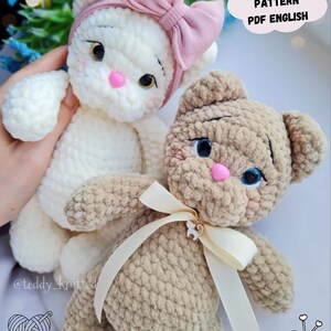 Puede incluir: Dos animales de peluche de ganchillo: un gato blanco con un lazo rosa y un oso marr&oacute;n con una cinta crema. Ambos tienen ojos azules y narices rosas. La imagen incluye el texto "CROCHET PATTERN PDF ENGLISH".
