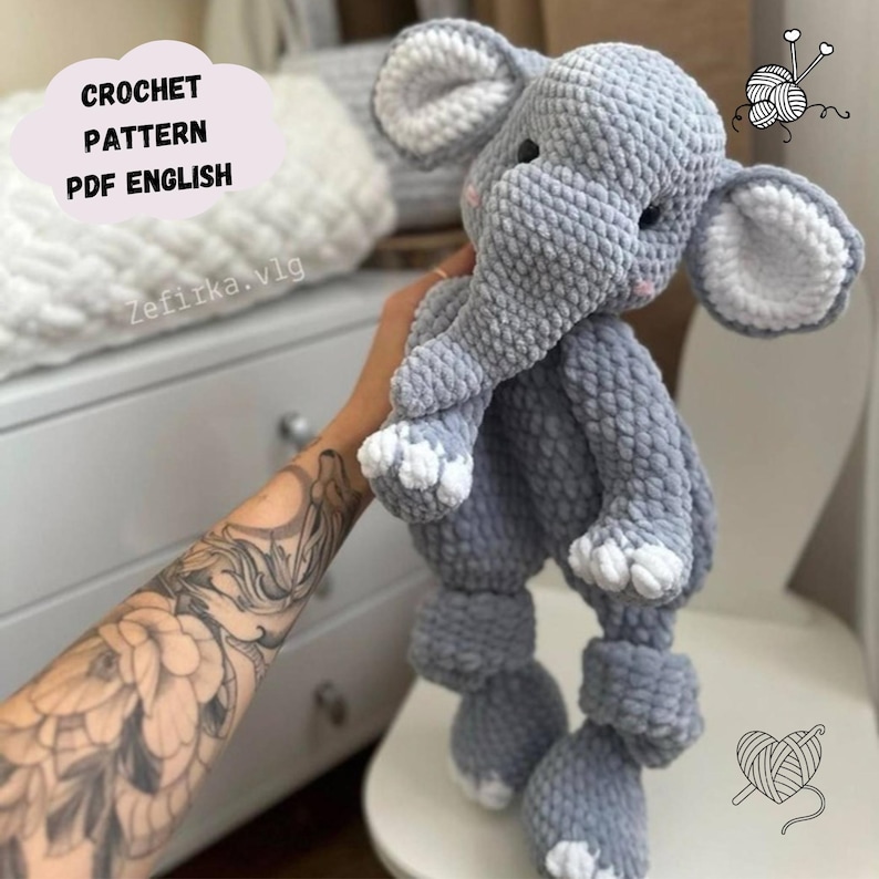 May include: A handmade gray crochet elephant toy with white accents on the ears and feet. The plush animal has a trunk, large ears, and is being held up. The image includes the text "CROCHET PATTERN PDF ENGLISH".