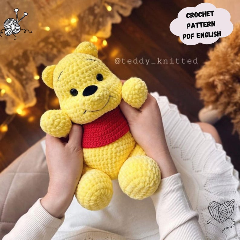 Op de afbeelding: Een gehaakt Winnie de Poeh knuffel in geel met een rood shirt. Het speelgoed wordt vastgehouden door de handen van een persoon. De tekst "CROCHET PATTERN PDF ENGLISH" en "@teddy_knitted" zijn zichtbaar in de afbeelding.