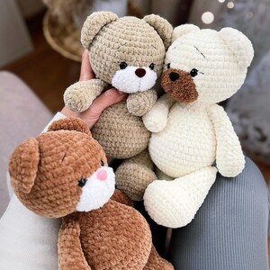 Op de afbeelding: Drie gehaakte teddyberen in verschillende kleuren: bruin, beige en wit. De beren hebben zwarte ogen en witte neuzen. De beren zitten op een grijs oppervlak met de tekst "jyk.toys" in wit.