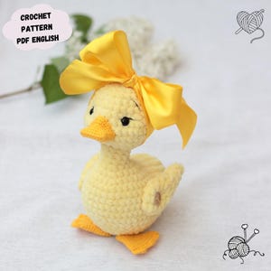 Peut inclure: Un caneton au crochet jaune fait &agrave; la main avec un n&oelig;ud jaune vif. Le caneton a un bec et des pieds jaunes. Le texte "CROCHET PATTERN PDF ENGLISH" est dans une zone de texte en forme de nuage. Un article charmant et fait &agrave; la main.