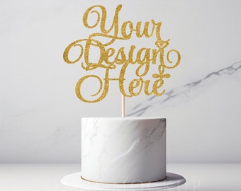 Może przedstawiać: Biały tort z ozdobą z  złotego brokatu, na której widnieje napis "Your Design Here".