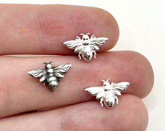 May include: Three small, silver-coloured bee charms with detailed wings and body segments. The bees are displayed on a light background, showcasing their intricate design. These charms are ideal for jewellery making or craft projects.
