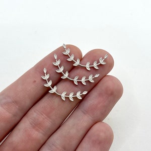 May include: Three silver-colored leaf branch charms. Each charm has a curved shape with small, detailed leaves. The charms are displayed against a white background, suggesting they are jewelry components or decorative elements.