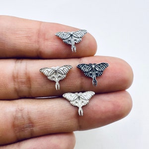 May include: Four small, silver-colored moth charms with detailed wing and body designs. The charms are displayed against a white background, showcasing their intricate patterns and textures. The moths are in various positions, highlighting their three-dimensional form.
