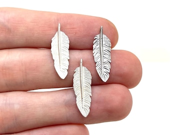 Op de afbeelding: Drie zilverkleurige veerkristallen. Elke bedel heeft een gedetailleerd veermotief met een centrale schacht en delicate weerhaken. De bedels zijn klein, ideaal voor het maken van sieraden of knutselprojecten.