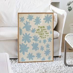 Puede incluir: Una impresión artística enmarcada con ilustraciones de flores azul claro sobre un fondo crema. La impresión incluye el texto "THERE ARE ALWAYS FLOWERS FOR THOSE WHO WANT TO SEE THEM". La obra de arte se exhibe en un salón.