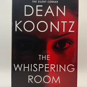May include: A hardcover book titled "The Whispering Room" by Dean Koontz. The cover features a red and black design with the author's name in large white letters. The title is also in white, with a woman's eye visible in the background.