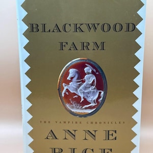 May include: A hardcover book titled Blackwood Farm by Anne Rice from The Vampire Chronicles series. The gold cover features a central oval cameo depicting a figure riding a horse, with white zigzag borders along the left and right edges.